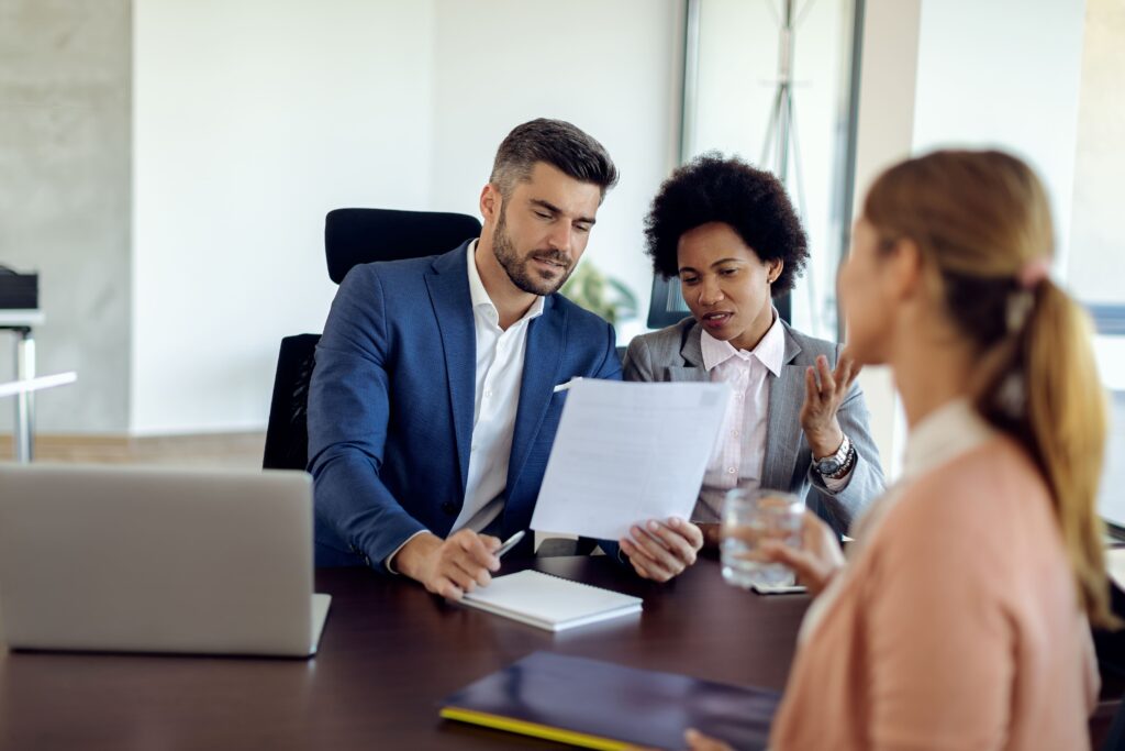 Imagem de três pessoas em torno de uma mesa de trabalho, um homem e duas mulheres. O homem está mostrando um documento para as colegas de trabalho. Imagem: Freepik.